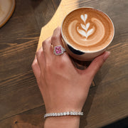 REINE pink radiant-cut gemstone ring worn on a hand holding a latte