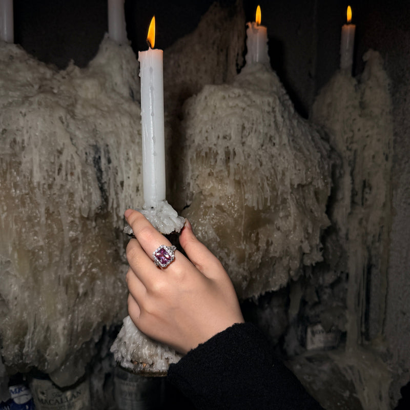 REINE pink-purple radiant-cut lab-grown gemstone ring with a moissanite halo, worn on a hand holding a candle.