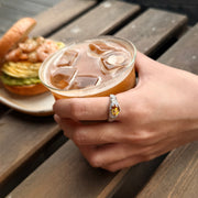 AUREL yellow oval gemstone ring worn on a hand holding an iced drink