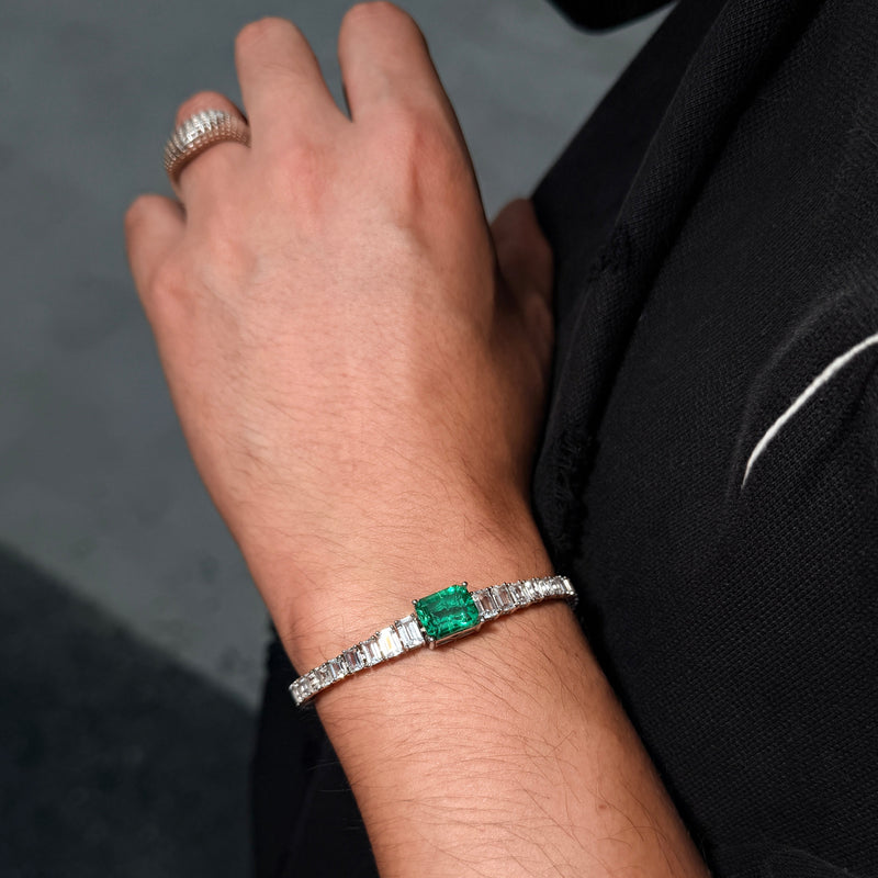 C?UR LAC tennis bracelet with a green emerald-cut lab-grown center stone, worn on the wrist with a black sleeve.