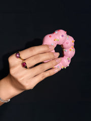 NOMI pink gemstone ring worn on a hand holding a pink doughnut