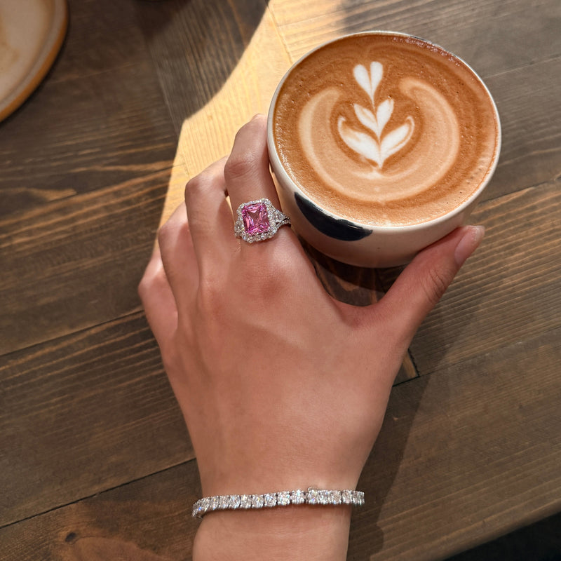 REINE pink radiant-cut gemstone ring worn on a hand holding a latte
